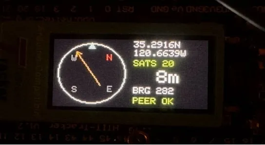 BuddyFinder handheld unit showing the live compass UI on its TFT display, with distance and bearing to the paired device